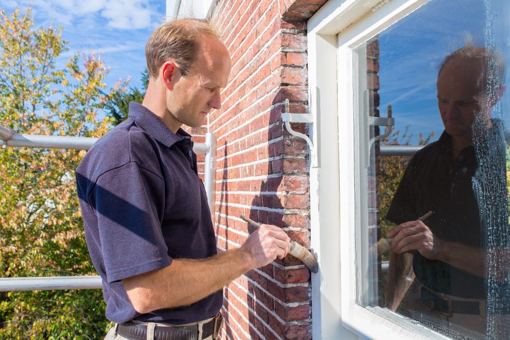Dutch painter paints window frame with brush